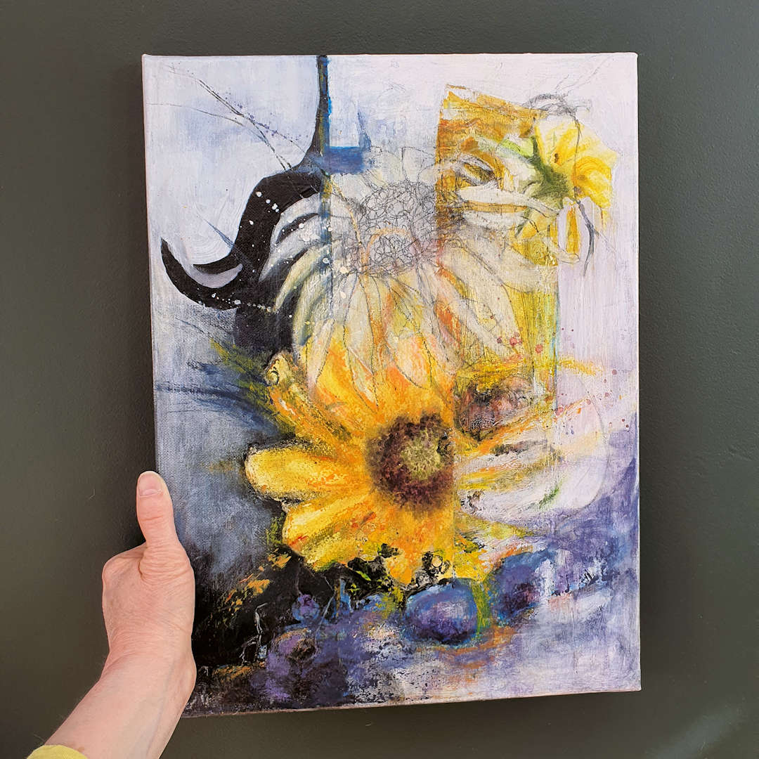 Sunflowers For Stacey being held in my hand against the wall. The abstract picture is joyful sunflowers